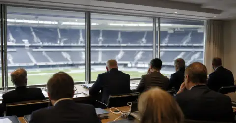Anonymous officials meet beside a view of an empty football stadium