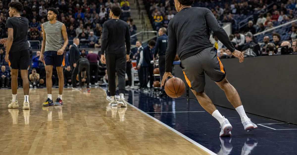 Anonymous basketball players warm up as a returning guard dribbles before tipoff.