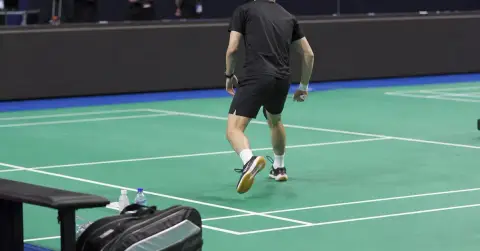 An anonymous badminton player practices alone on a quiet indoor court.