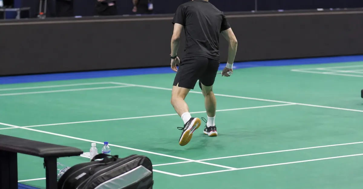 An anonymous badminton player practices alone on a quiet indoor court.