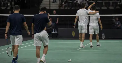 Badminton doubles players regroup at the net after a close match.