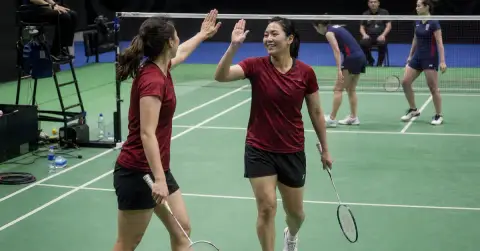 Two badminton partners celebrate near the net after winning a doubles match.