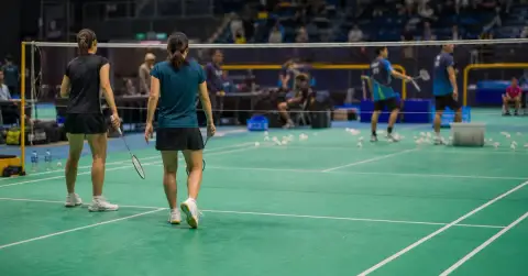 Anonymous badminton doubles pair celebrate a point in a crowded indoor arena.