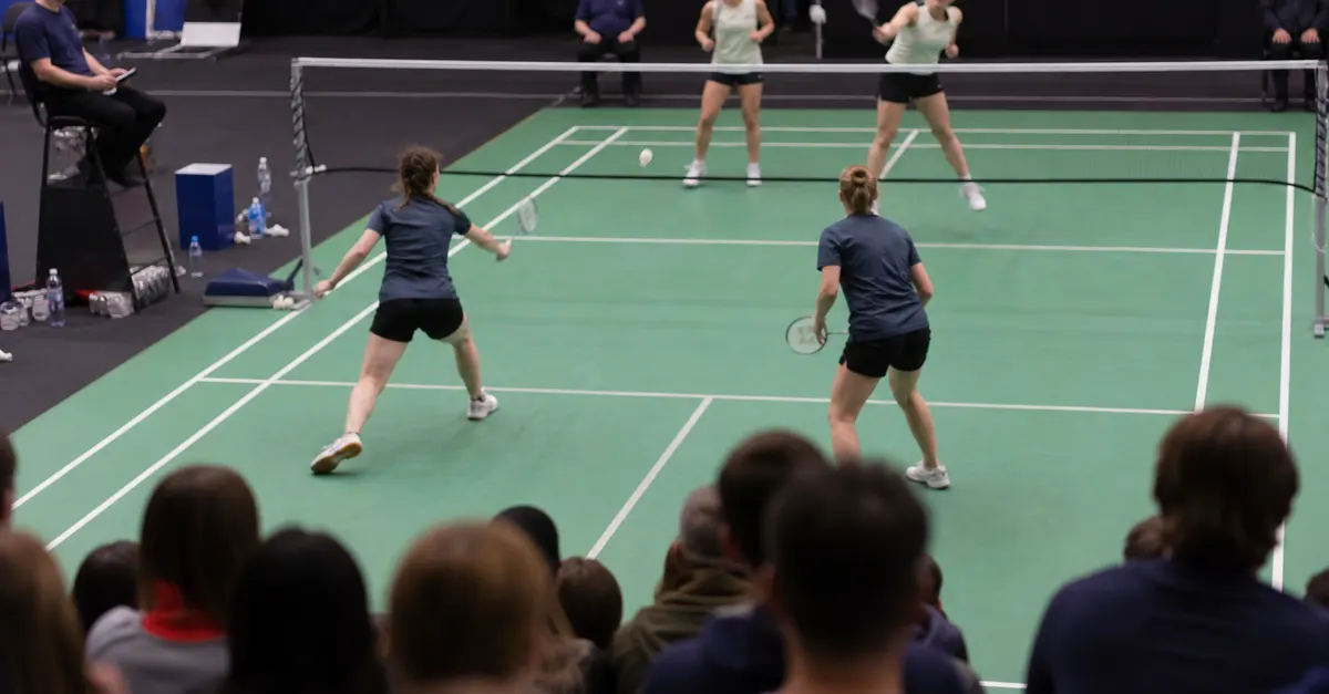 Four anonymous badminton players contest a rally at an indoor tournament.