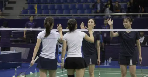 Women’s badminton doubles players meet opponents at the net after a match.