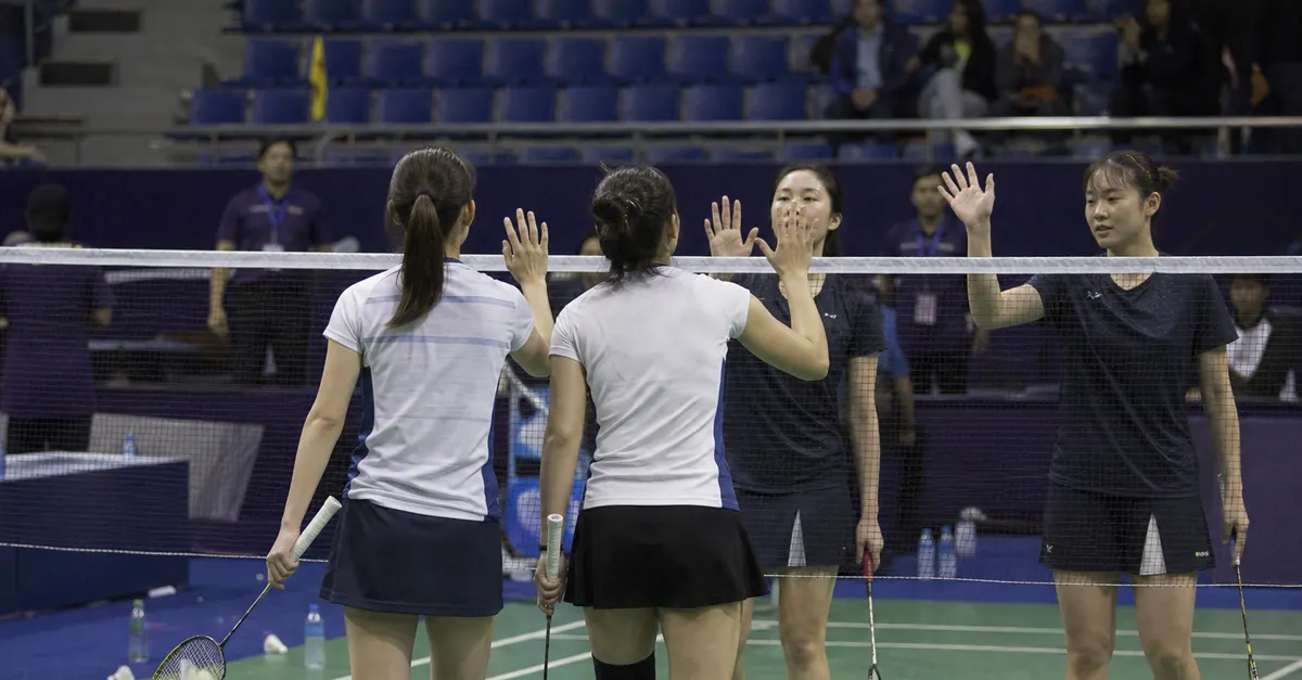 Women’s badminton doubles players meet opponents at the net after a match.