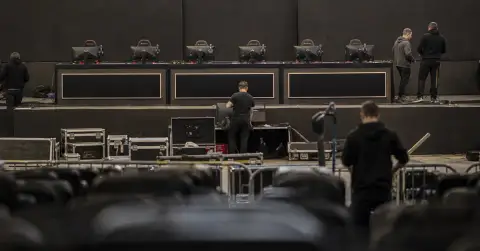 Technicians prepare a sparse esports stage with six gaming stations.