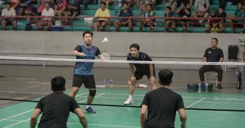 Four anonymous badminton players contest a doubles rally on an indoor court.