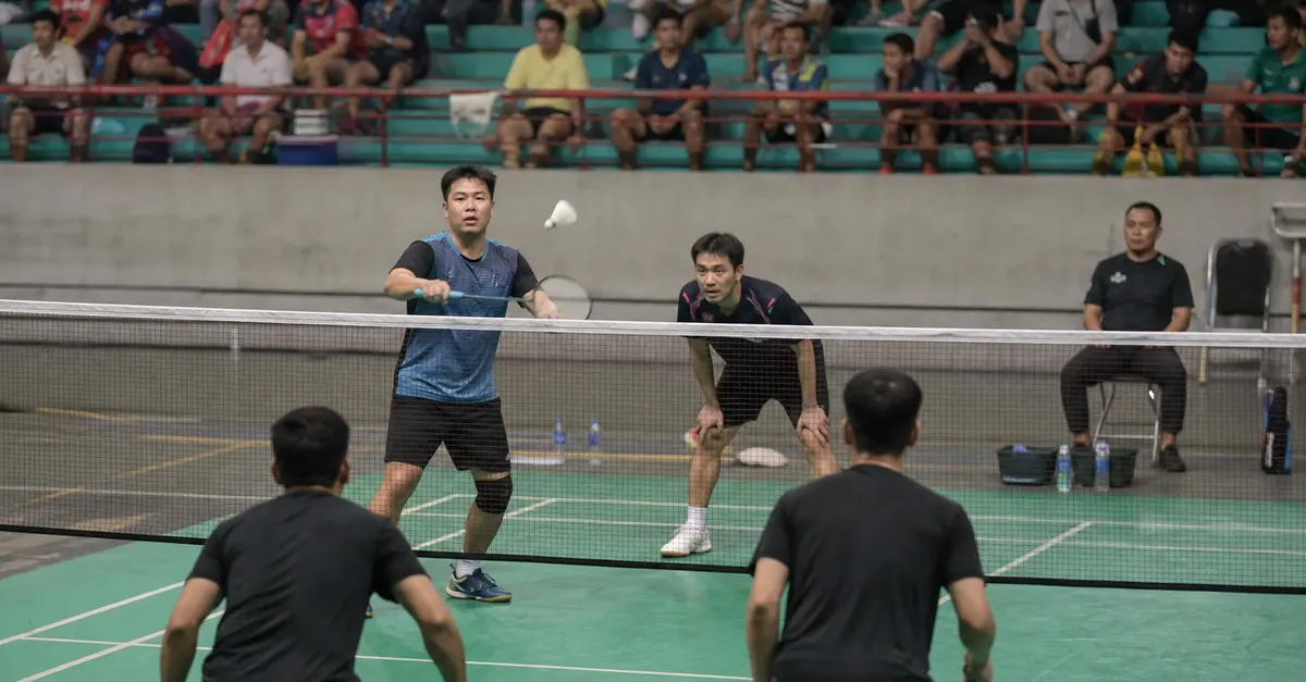 Four anonymous badminton players contest a doubles rally on an indoor court.