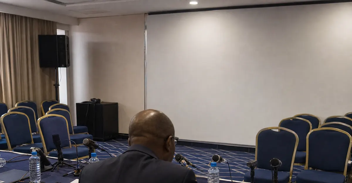 Anonymous official at a football federation briefing table in a plain room