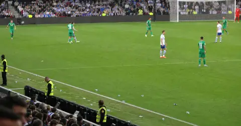 Football match halted as scattered objects lie near the touchline