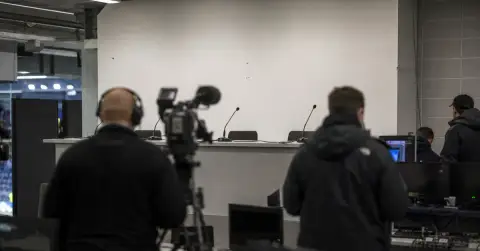 Empty football press room with cameras and inactive broadcast monitors.