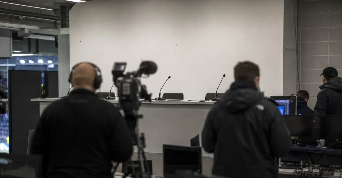 Empty football press room with cameras and inactive broadcast monitors.