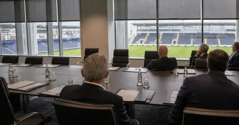 Anonymous football executives meet amid empty chairs and folders