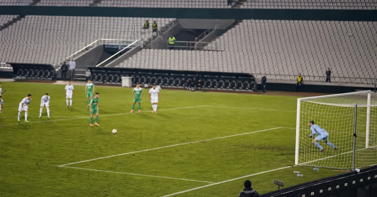 Anonymous players contest a tense football match in an empty stadium.