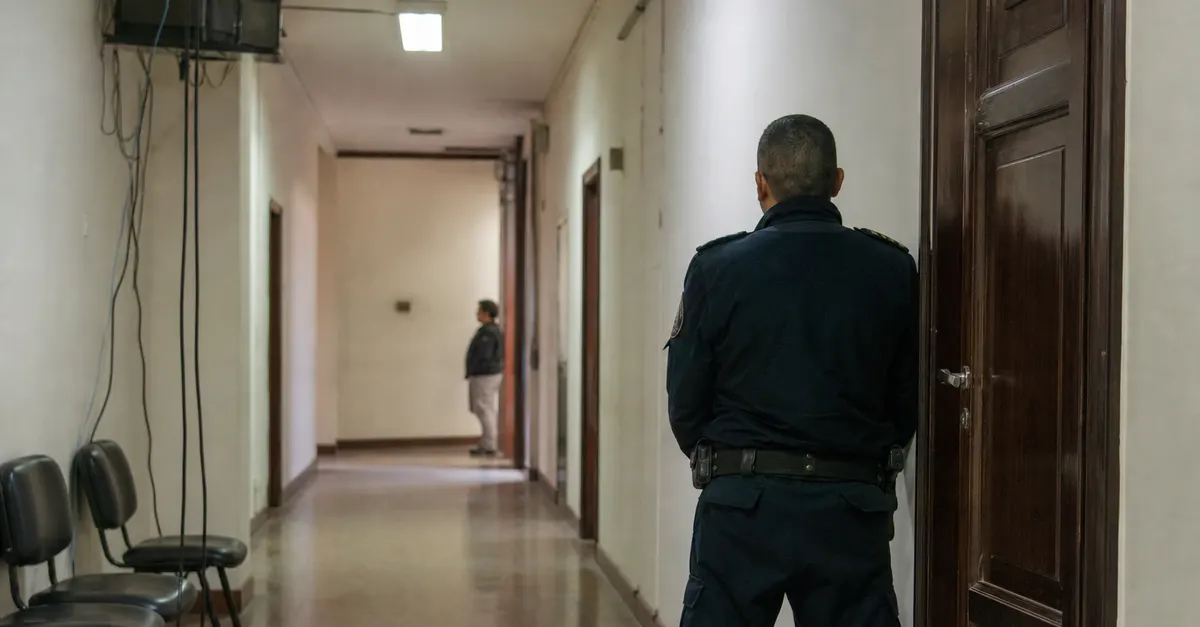 A quiet courthouse corridor with security outside a closed courtroom.