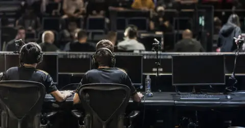 Two esports players join teammates at gaming PCs in an arena