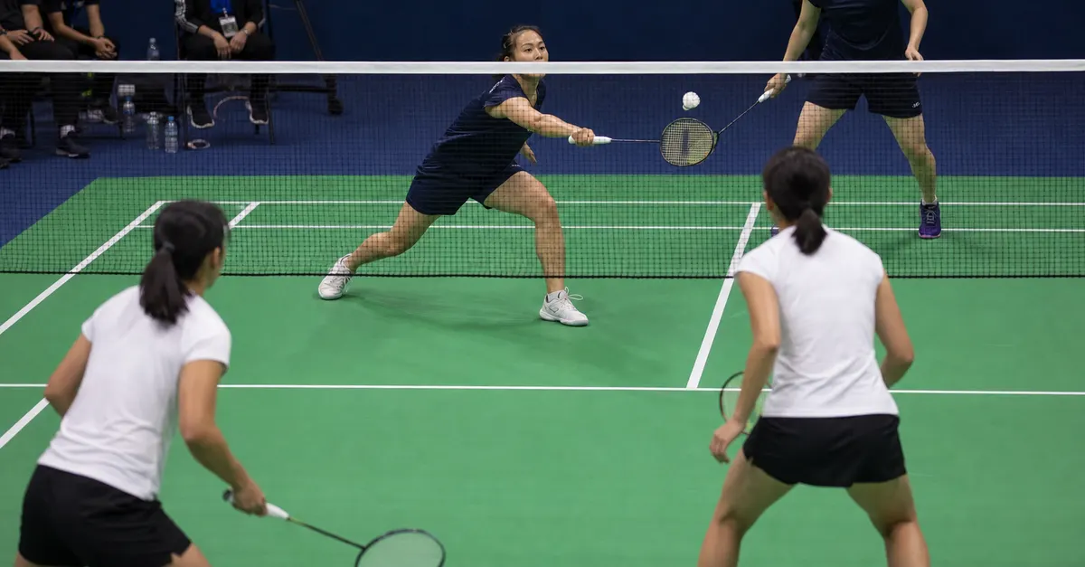 Four anonymous badminton players contest a doubles rally on an indoor court.