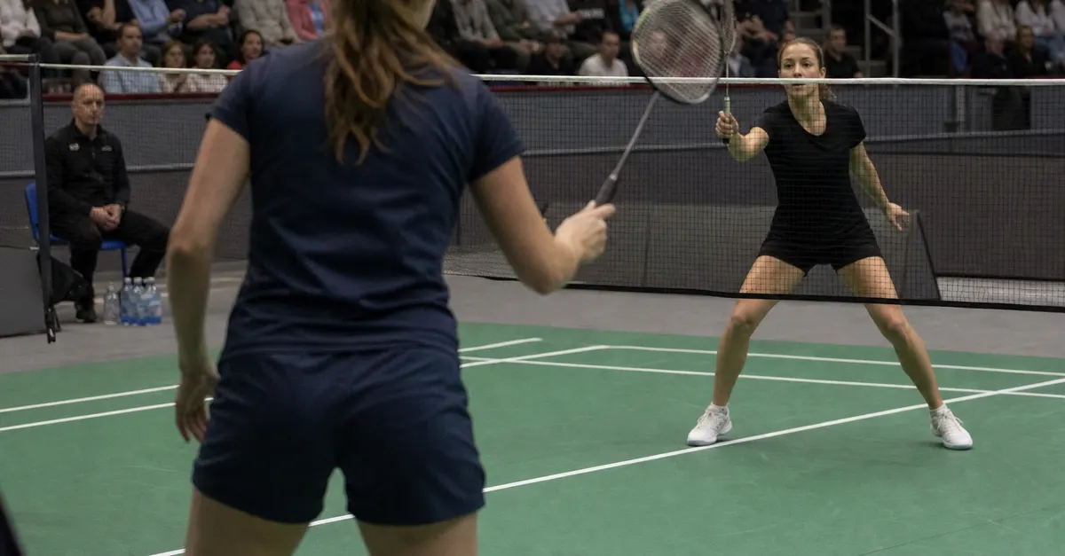 Two anonymous badminton players face each other across a net.