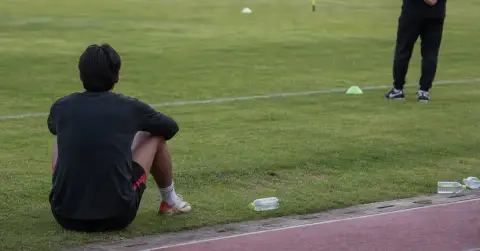 An isolated footballer sits near the touchline during a quiet training session.