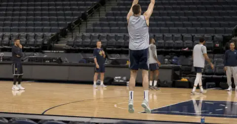 A tall basketball player practices a shot in an empty arena.