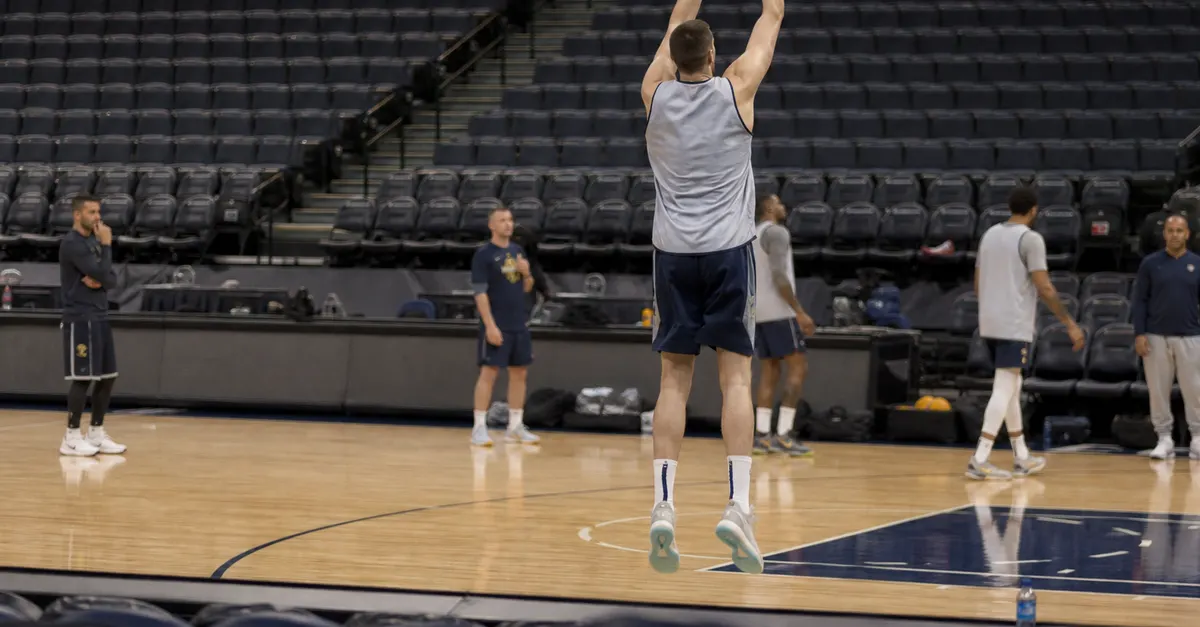 A tall basketball player practices a shot in an empty arena.
