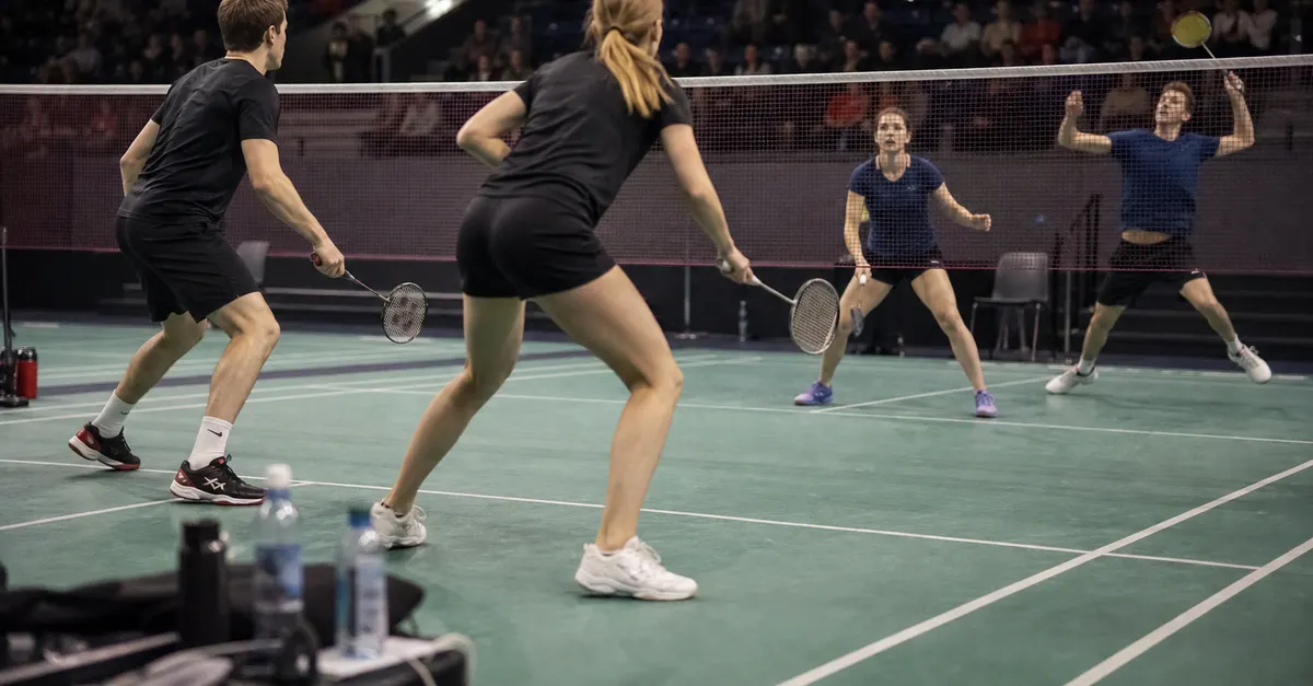 Anonymous mixed doubles badminton players compete on an indoor court.