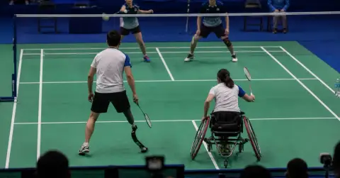 Anonymous para-badminton mixed doubles pair contest a rally in an indoor arena.