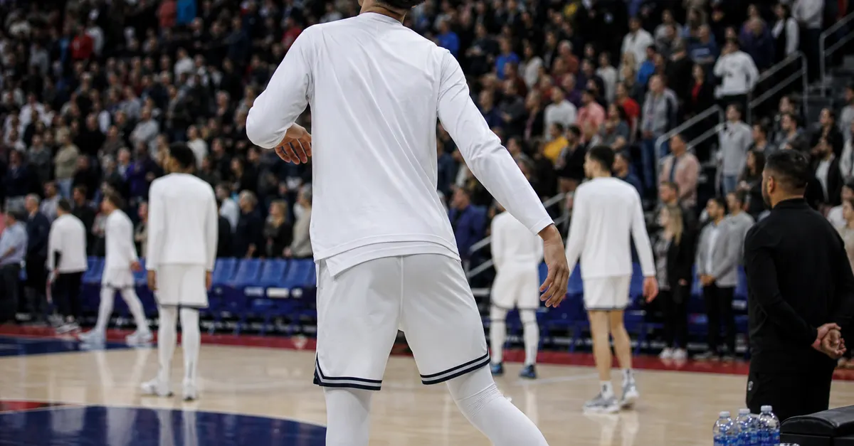 Anonymous basketball players warm up as spectators stand in an arena.