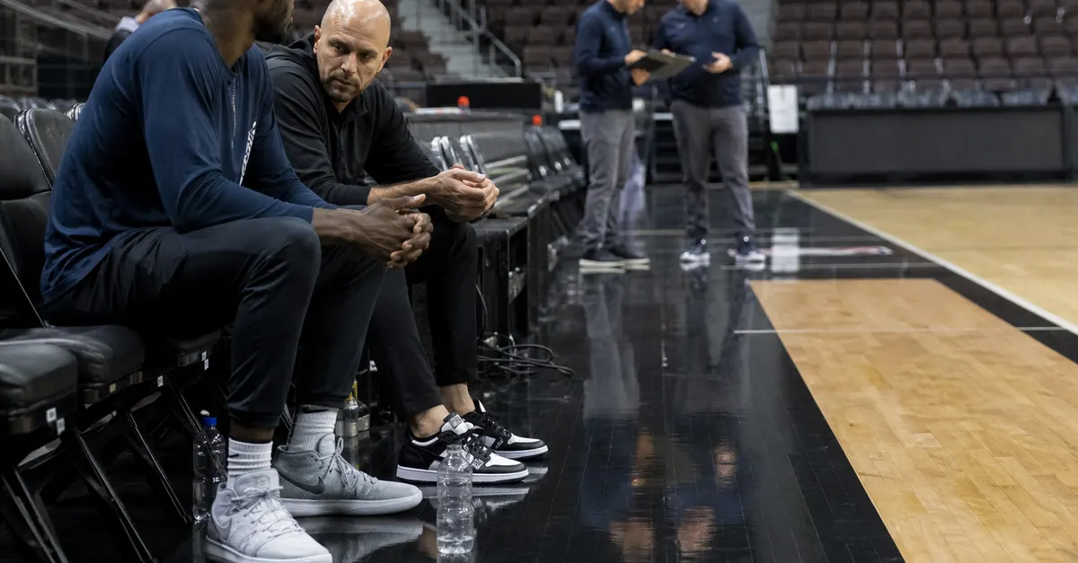 Anonymous basketball player sits courtside as staff discuss a possible roster move.