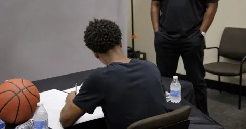 Anonymous basketball player signs paperwork at a plain press-room table