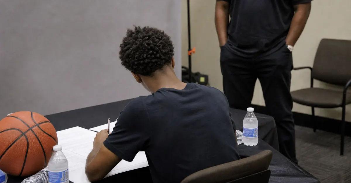 Anonymous basketball player signs paperwork at a plain press-room table