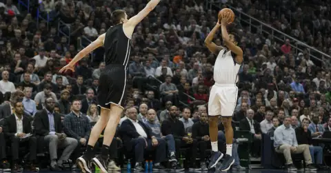 A tall defender contests a shorter guard’s jump shot during a basketball game.