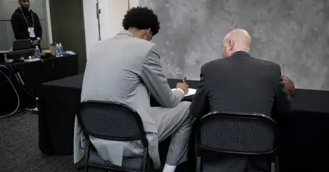 Tall anonymous basketball player signs a contract in a plain press room