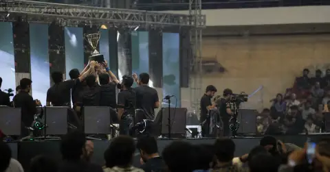 Anonymous esports players celebrate onstage beside a plain championship trophy.