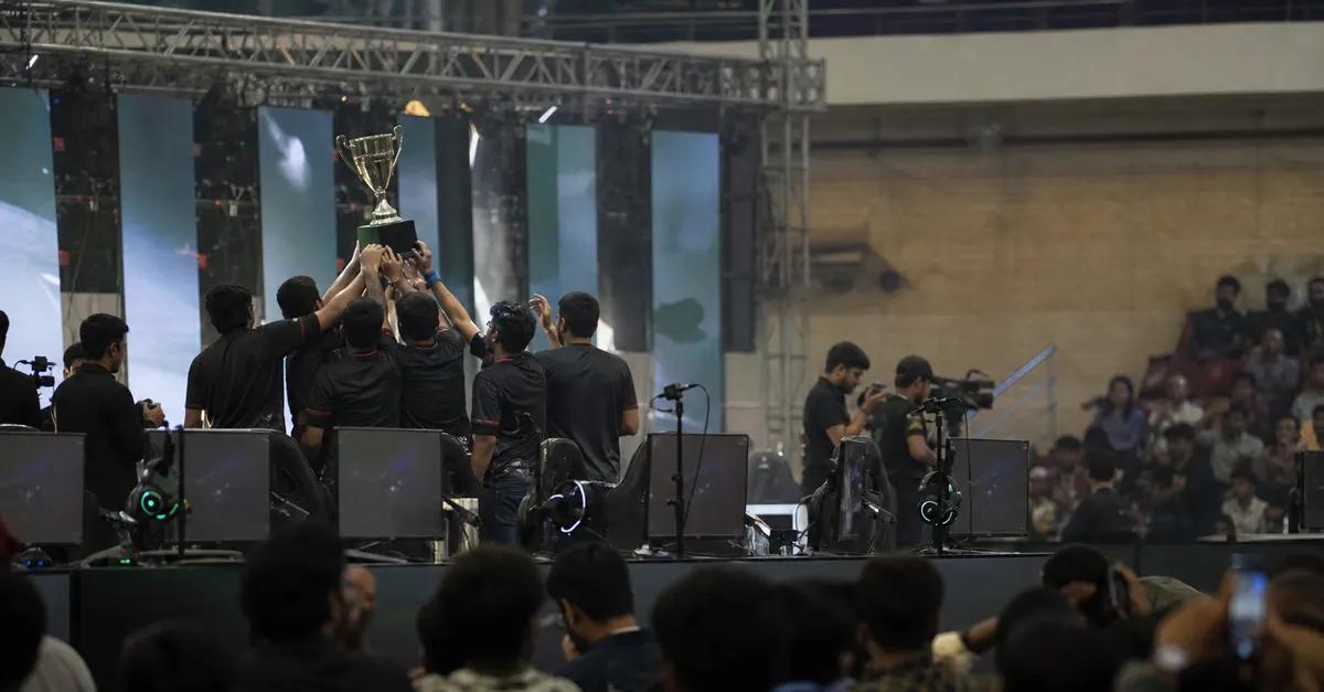 Anonymous esports players celebrate onstage beside a plain championship trophy.