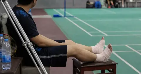 A badminton player rests with both feet bandaged beside a court.