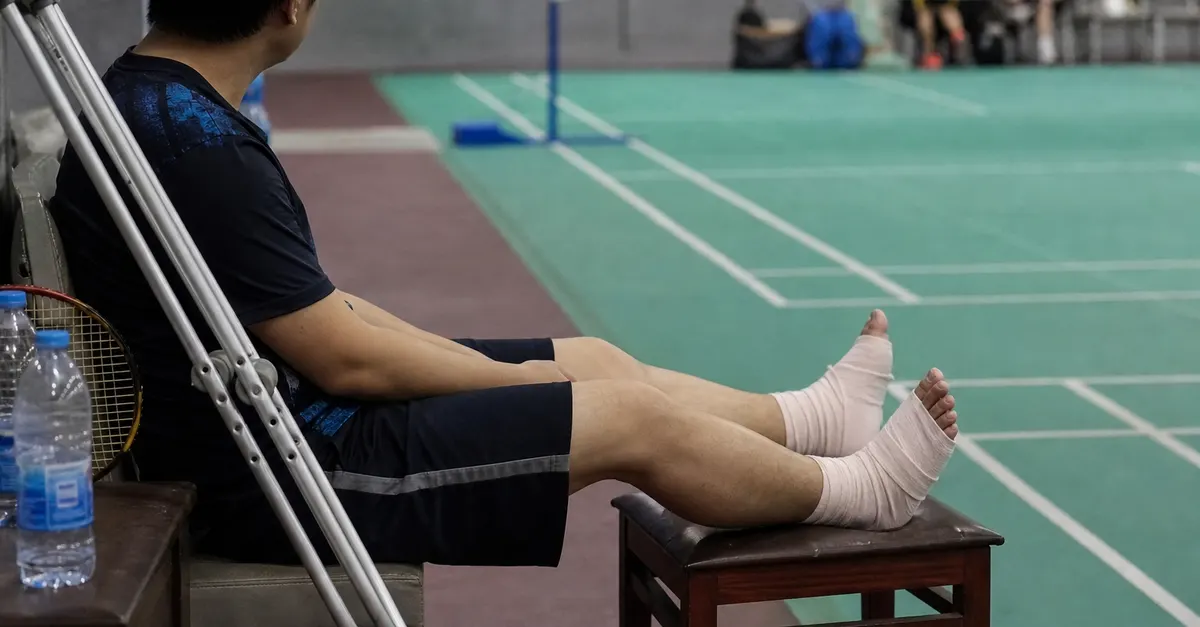 A badminton player rests with both feet bandaged beside a court.