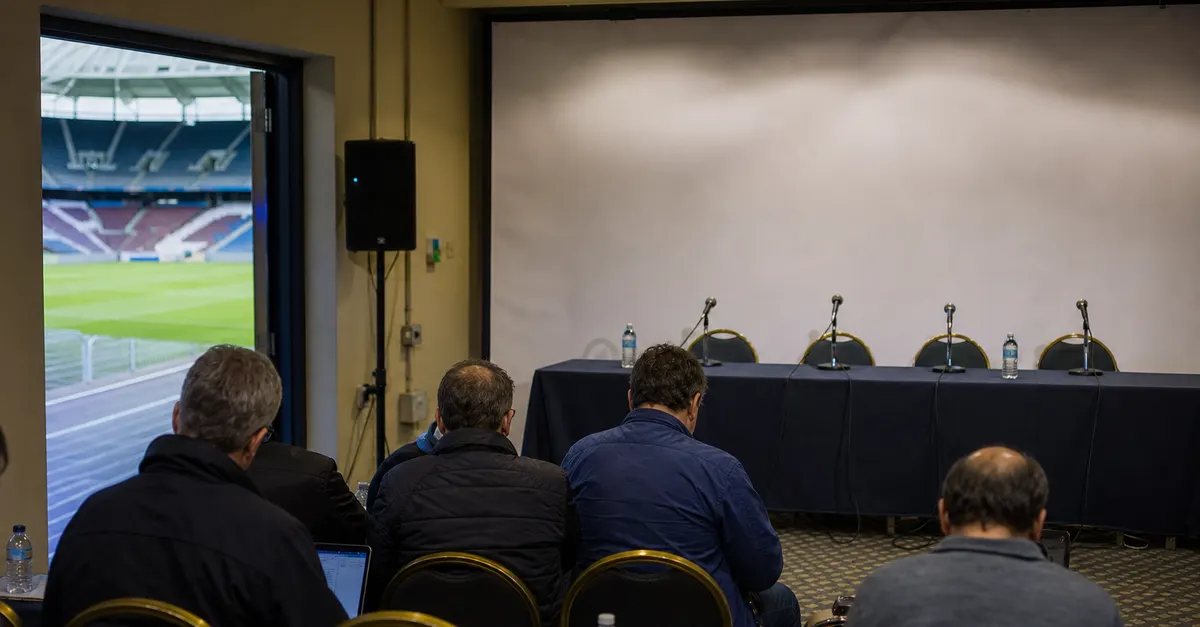 Anonymous football officials meet in a plain press room beside an empty stadium.